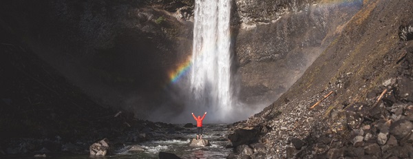 mann steht vor wasserfall mit regenbogen